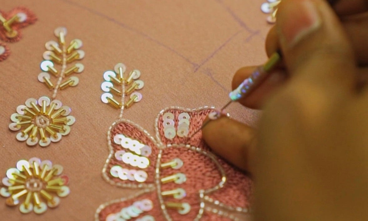 Hand applying sequins to a decorative card with floral designs.